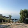Sentiero sterrato con vista sul mare calmo, circondato da alberi e rocce.