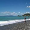 Spiaggia di ciottoli con bagnanti e mare calmo, cielo sereno con poche nuvole.