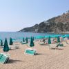 Spiaggia sabbiosa con lettini e ombrelloni verdi, mare calmo sullo sfondo.