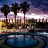 Piscina illuminata al tramonto con palme.